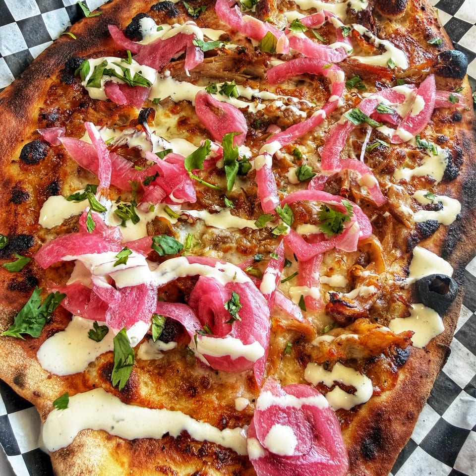 Flatbread pizza with chicken, pickled red onions, cilantro, and white sauce on checkered paper.