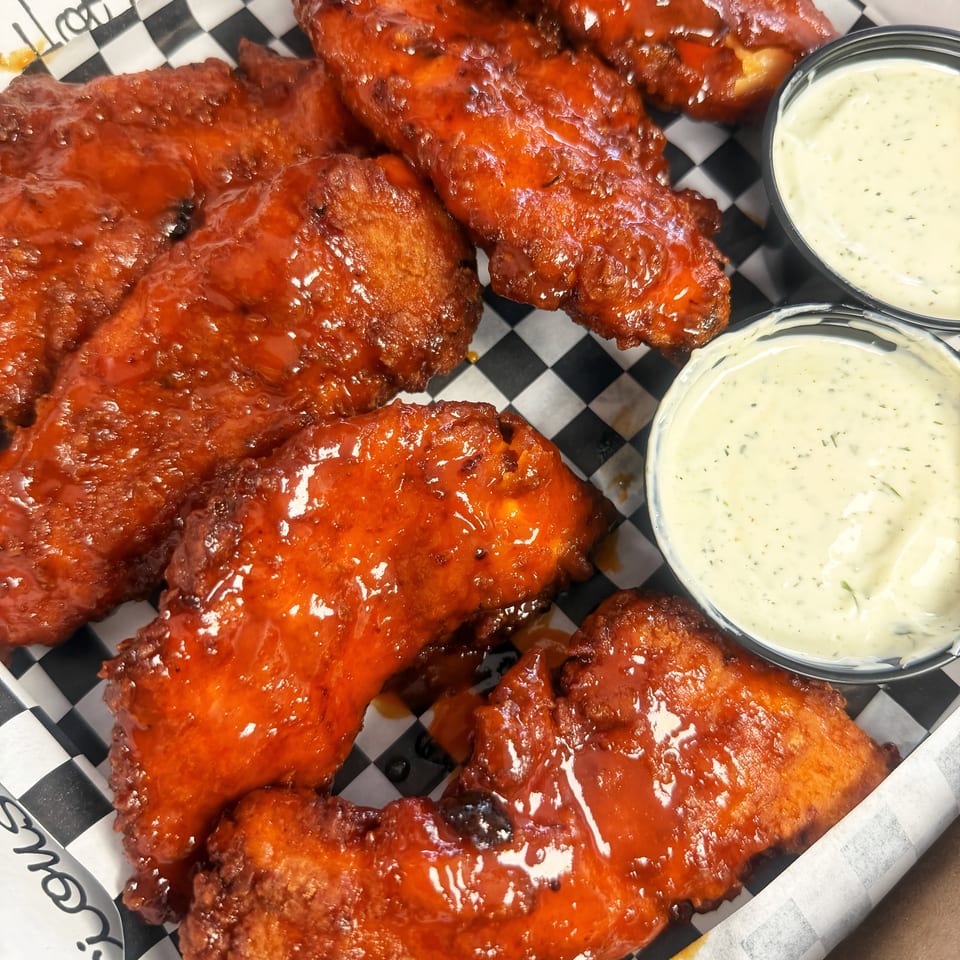 Spicy orange chicken tenders with two cups of creamy dipping sauce in a checkered paper-lined box.