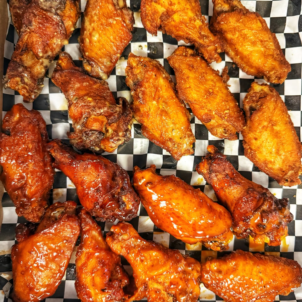 A box of Delicious Pizza chicken wings, some plain and some coated in barbecue sauce.